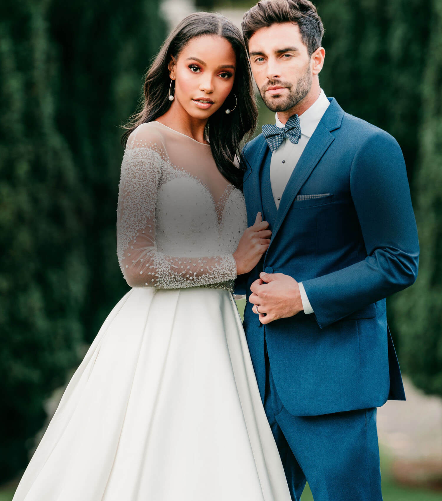 Сouple wearing a white gown and a dark blue suit. Mobile image